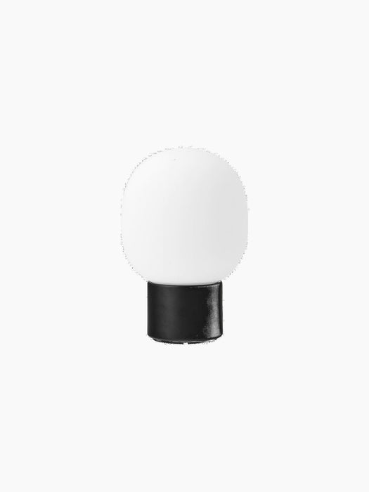 JWDA Table Lamp, Portable, in black, seen from the back. It features a solid black cylindrical base and a white glass shade.