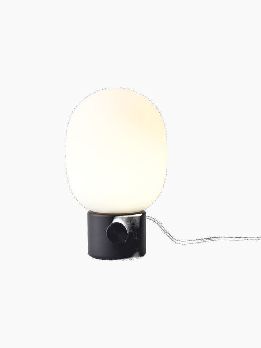A front view of the JWDA Table Lamp, Small, in black painted steel with its illuminated white opal glass shade.