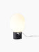 A front view of the JWDA Table Lamp, Small, in black painted steel with its illuminated white opal glass shade.