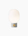 Front view of the JWDA Table Lamp, Small, with a light grey concrete base, brass dimmer knob, and lit opal glass shade.