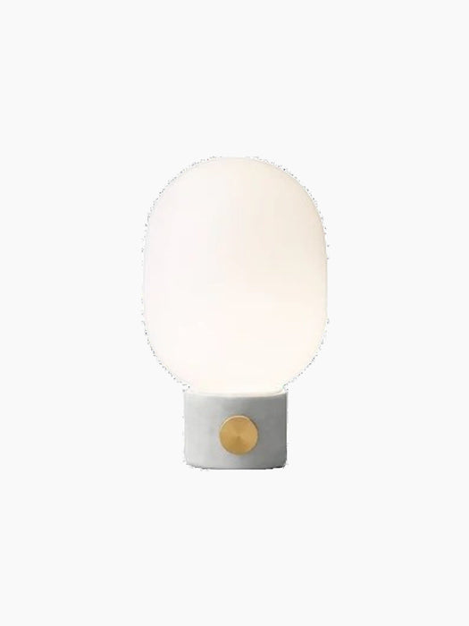 JWDA Table Lamp, Small, with a light grey concrete base, circular brass dimmer, and an illuminated opal glass shade.