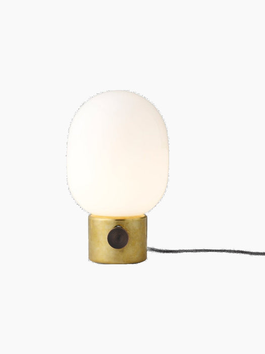 Front view of the JWDA Table Lamp, Small, with a polished brass base and glowing opal glass shade against a black background.