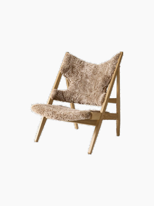 Angled view of the Knitting Lounge Chair, featuring Sahara sheepskin upholstery with elbow cut-outs and a natural oak frame.
