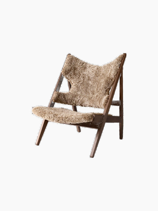 Angled view of the Knitting Lounge Chair with a dark-stained oak frame and Sahara sheepskin upholstery with elbow cutouts.