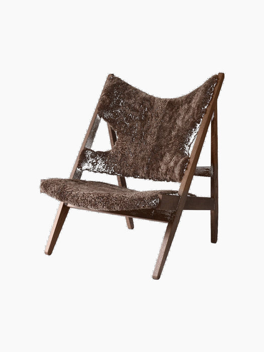 An angled view of the Knitting Lounge Chair, showing its dark stained oak frame and warm brown sheepskin seat and back.
