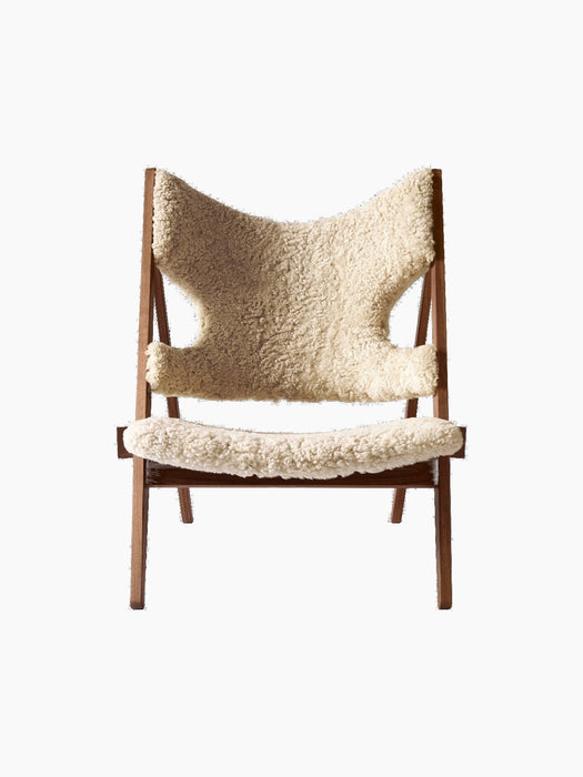 A front view of the Knitting Lounge Chair, featuring a dark walnut wood frame and upholstered in fluffy, natural sheepskin.