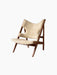 Knitting Lounge Chair in natural sheepskin and a walnut frame, shown from a three-quarter angle on a dark background.