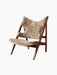 The Knitting Lounge Chair has a dark walnut A-frame with a seat and winged backrest upholstered in textured beige sheepskin.