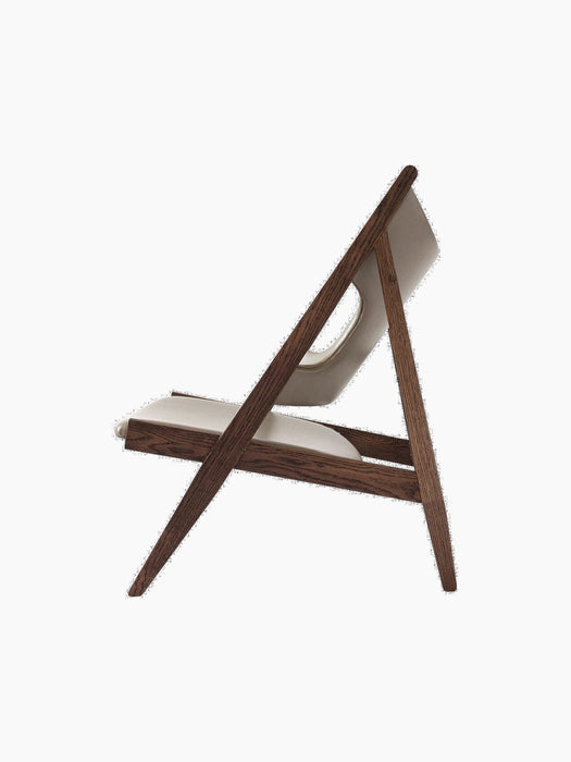 A side profile of the Knitting Lounge Chair with a dark stained wood frame and light beige leather seat and backrest.