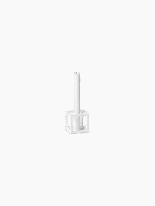 A white Kubus 1 candlestick holder, with its geometric cube design, holding a single white candle against a black background.