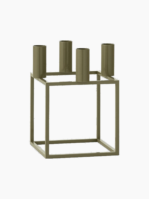 The Kubus 4 candle holder in olive green, shown at an angle. It has a geometric, square metal frame and four candle holders.