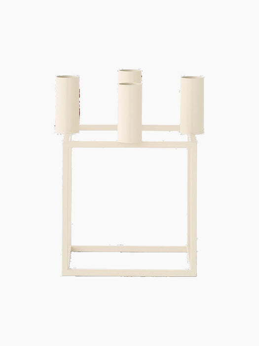 A front view of the ivory Kubus 4 candle holder, a square metal frame with four cylindrical holders for taper candles.