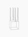 A white Kubus 4 candle holder with a geometric cube base, holding four tall, white, unlit candles against a black background.