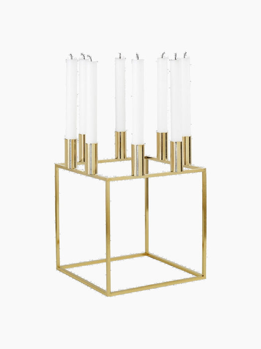 A gold-plated Kubus 8 candle holder with a square frame, holding eight unlit white candles, shown from an angle.