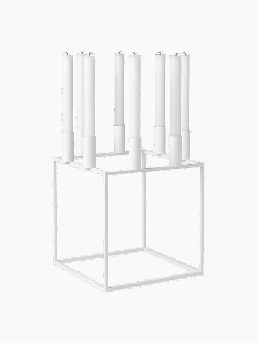 A white Kubus 8 candle holder with a minimalist cube frame, holding eight tall white candles on a black background.