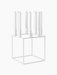 A white Kubus 8 candle holder with a minimalist cube frame, holding eight tall white candles on a black background.
