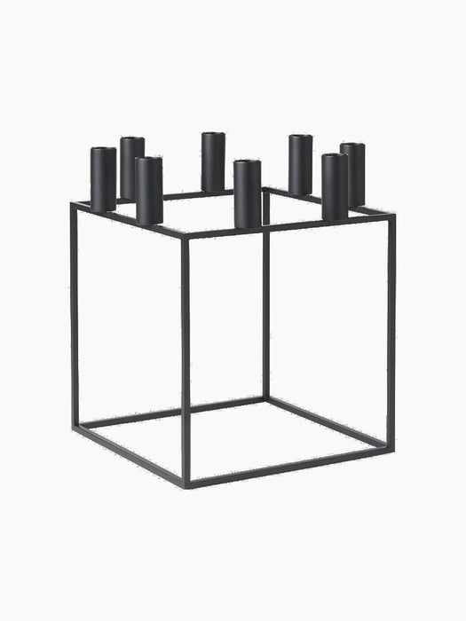 The black metal Kubus 8 candle holder, a minimalist cube frame with eight cylindrical holders for candles.