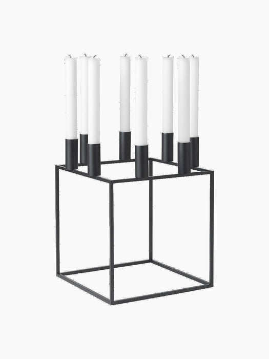 The Kubus 8 candle holder in black, a minimalist, cube-shaped metal frame holding eight tall white candles.