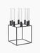 The Kubus 8 candle holder in black, a minimalist, cube-shaped metal frame holding eight tall white candles.