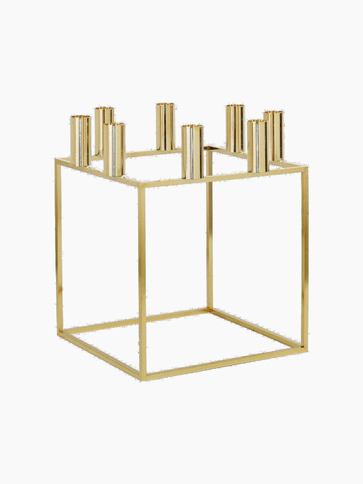 The gold-plated Kubus 8 candle holder, shown from an angle. It has a square, minimalist frame with 8 candle sockets on top.