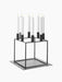A black metal Kubus 8 candle holder with eight lit white candles, shown on the matching square Base for Kubus 8.