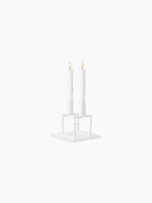 A white Kubus Line candle holder with two lit candles sitting atop the matching Kubus Base, shown against a black background.