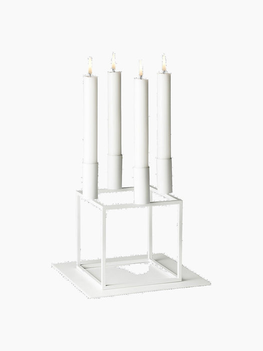 White Kubus 4 candelabra with four lit white candles, shown on the matching white Kubus Base against a black background.