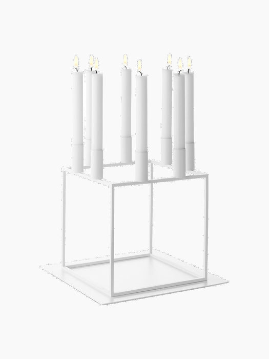 A white, geometric Kubus 8 candle holder with eight lit candles, resting on its matching square white Base for Kubus 8.
