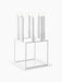 A white, geometric Kubus 8 candle holder with eight lit candles, resting on its matching square white Base for Kubus 8.