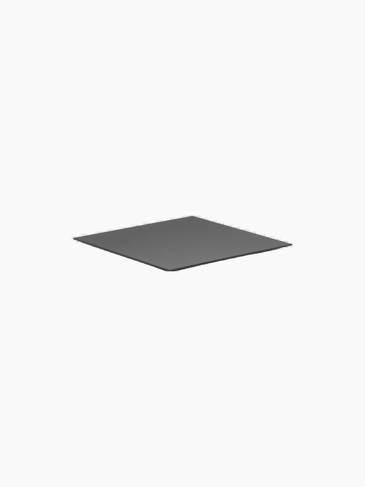 A thin, square, black metal base for the Kubus 4 candleholder, displayed at an angle against a stark black background.