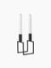 A black, geometric Kubus Line candle holder with two tall white candles, viewed from an angle against a black background.