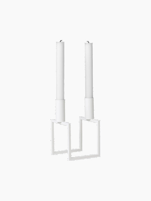 An angled view of the white Kubus Line candlestick, a minimalist design with a geometric frame, holding two white candles.