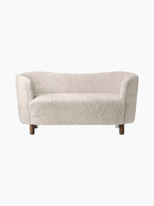 Front view of the Mingle Sofa in Moonlight sheepskin, with a curved back and dark stained oak legs on a black background.