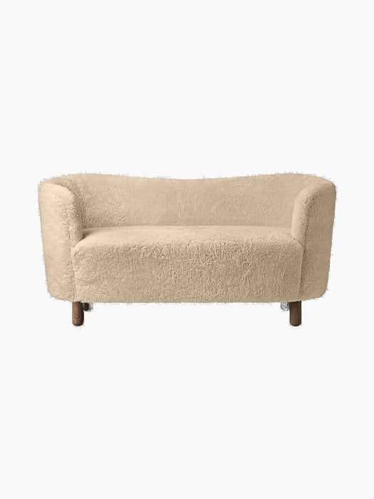 A front view of the Mingle Sofa, upholstered in Honey-coloured sheepskin, with dark stained oak legs, on a black background.