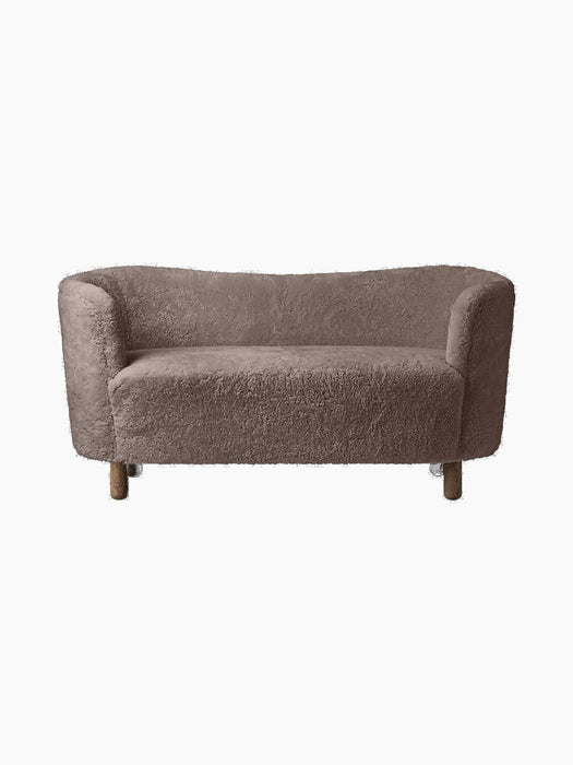 A front view of the Mingle Sofa, upholstered in Sahara-coloured sheepskin, with a curved back and dark-stained oak legs.