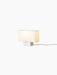 An angle view of the illuminated Nonna Table Lamp, featuring a rectangular sand-coloured textile shade on an aluminium base.