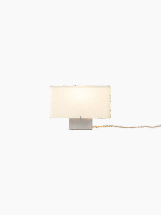 Front view of the illuminated Nonna Table Lamp with its rectangular, sand-coloured shade and brushed aluminium base.