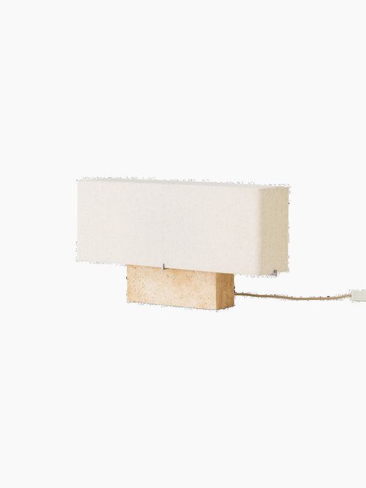 Side view of the wide Nonna Table Lamp with a rectangular travertine base and sand-coloured linen shade, shown switched off.