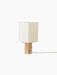 Angled view of the Nonna Table Lamp, off. It features a rectangular travertine base and a square, sand-hued shade.