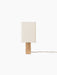 Front view of the switched-off Nonna Table Lamp, showing its rectangular travertine base and sand-coloured linen shade.