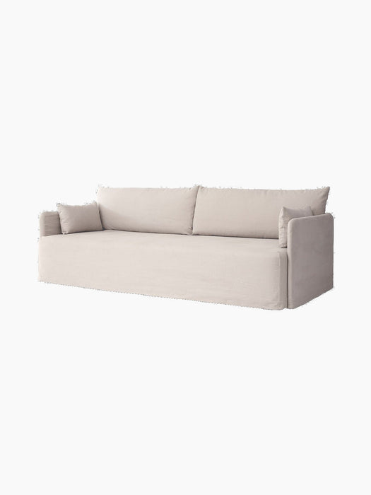 A light-coloured three-seater Offset Sofa w. Loose Cover with two large back cushions and two smaller pillows at the arms.