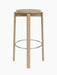 A front-on view of the Passage Bar Stool in natural oak, featuring a round seat, four legs, and a stainless steel footring.