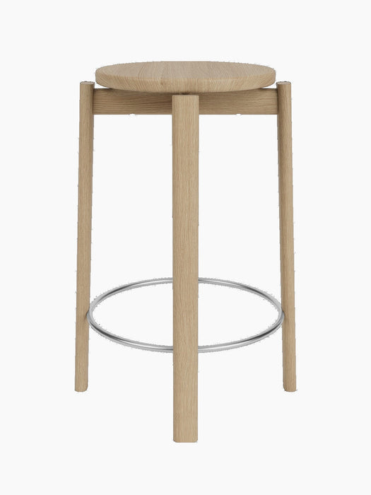 A front view of the Passage Counter Stool in natural oak, showing its round seat, three legs, and stainless steel footrest.