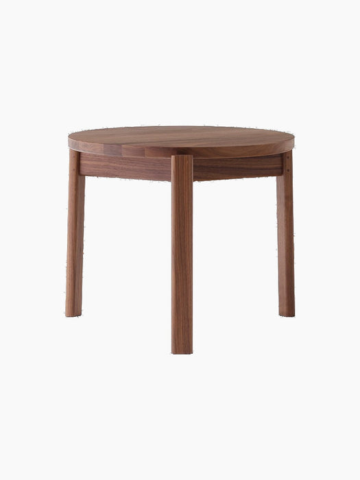 A Passage Lounge Table in dark walnut wood, shown from the front on a black background, with a round top and three legs.