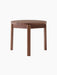 A Passage Lounge Table in dark walnut wood, shown from the front on a black background, with a round top and three legs.