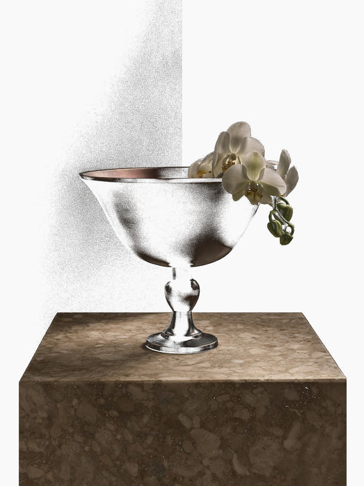 The Audo Pavot Bowl in a dark bronze finish, displayed on a marble block with a white orchid draped over its edge.