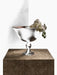 The Audo Pavot Bowl in a dark bronze finish, displayed on a marble block with a white orchid draped over its edge.