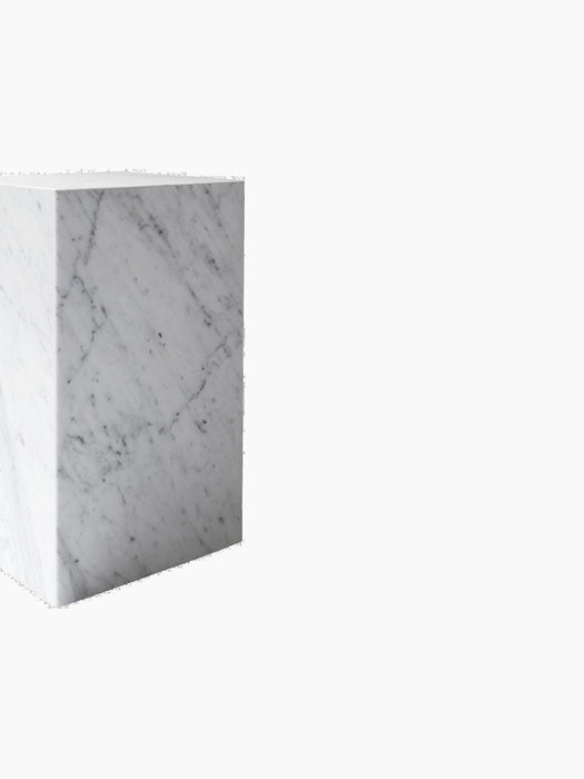 A close-up view of the Audo Plinth Tall in white marble, showing its elegant grey veining against a black background.