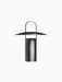 A front-on view of the black Ray Table Lamp, Portable. The lamp has a cylindrical base, a wide, disc-like shade, and a handle