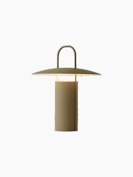 Angled view of the lit Ray Table Lamp, Portable, in dusty green. The lamp has a cylindrical base, a wide shade, and a handle.